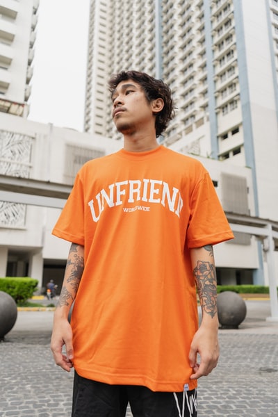身着橙色圆领t恤的男子白天站在黑色圆球附近
